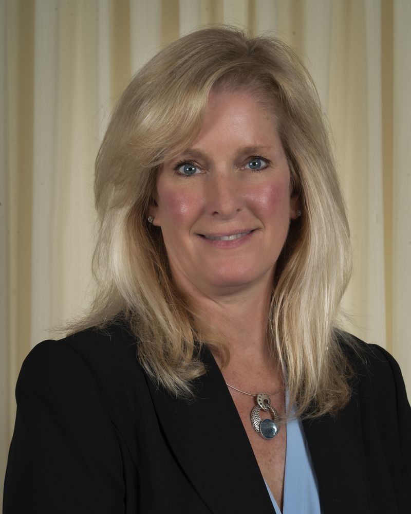A woman in a black jacket and blue shirt is smiling for the camera.