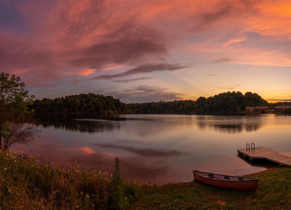 A wooden walkway leading to a gazebo overlooking a body of water at sunset.