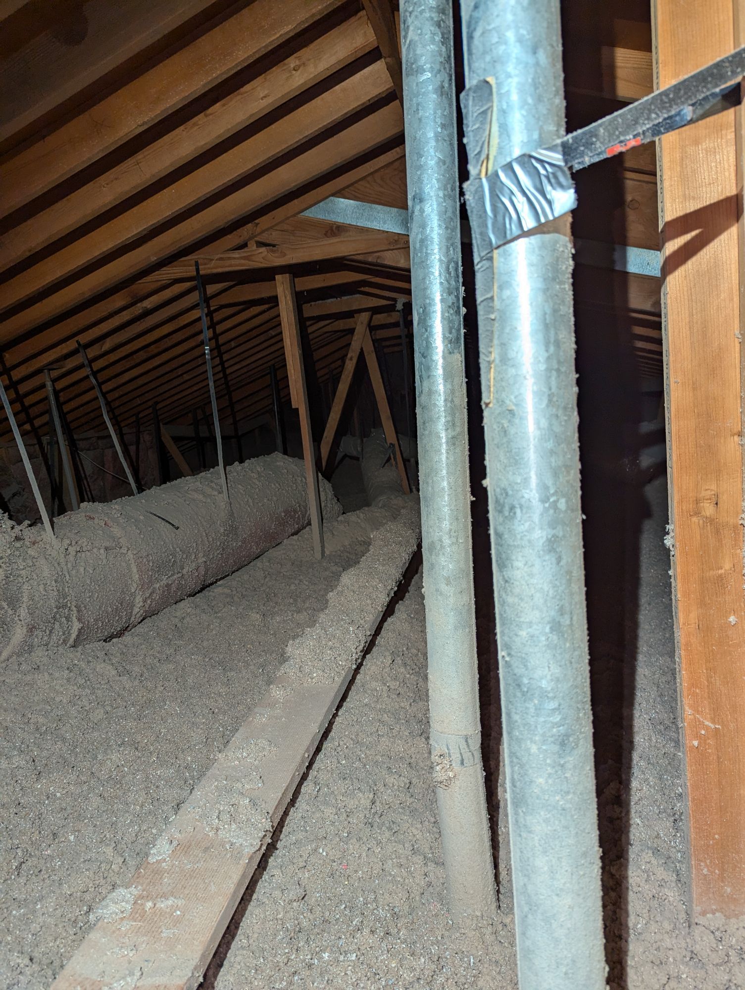 A dark attic with a lot of pipes and wooden beams.