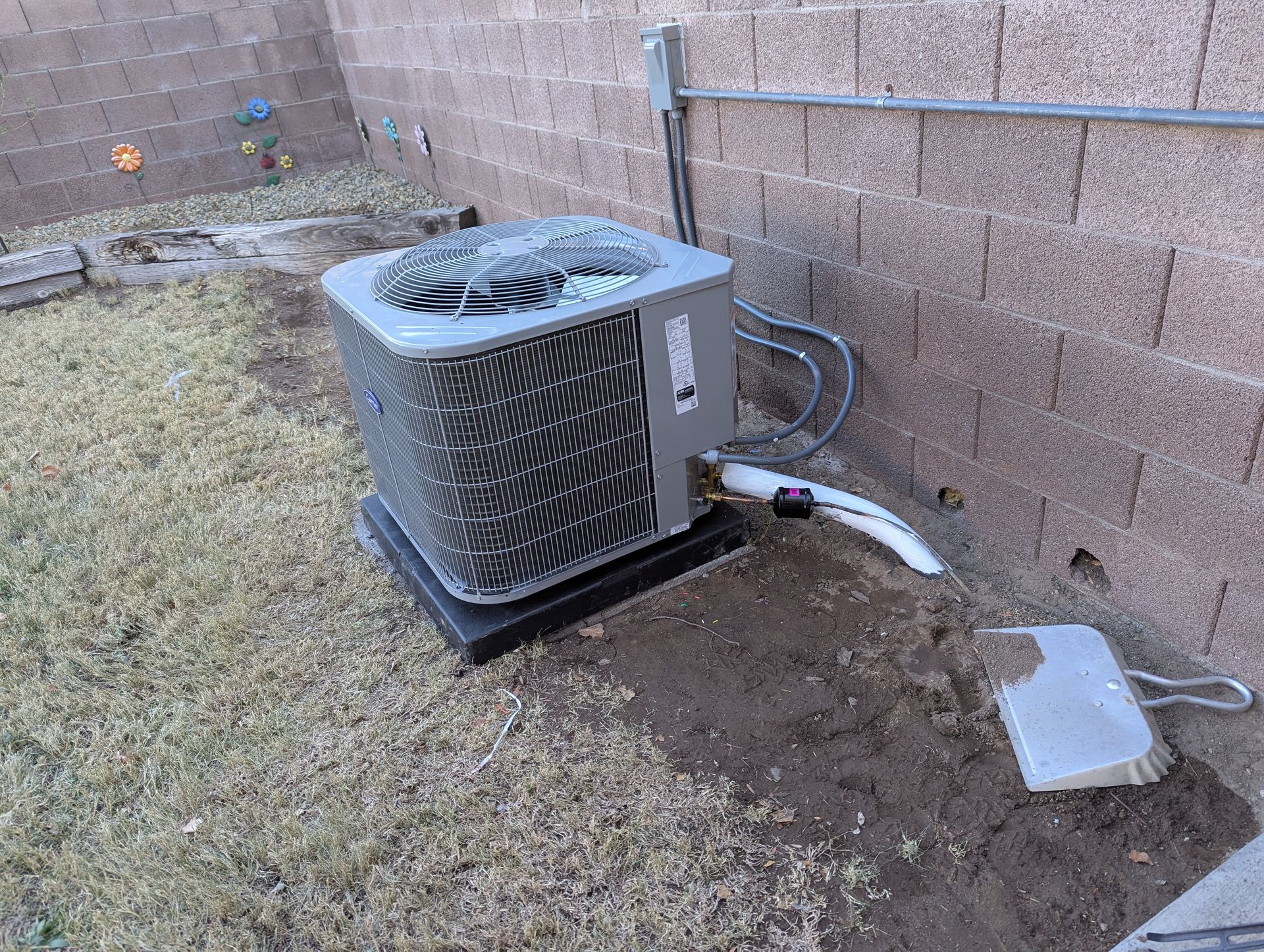 An air conditioner is sitting in the dirt next to a brick wall.