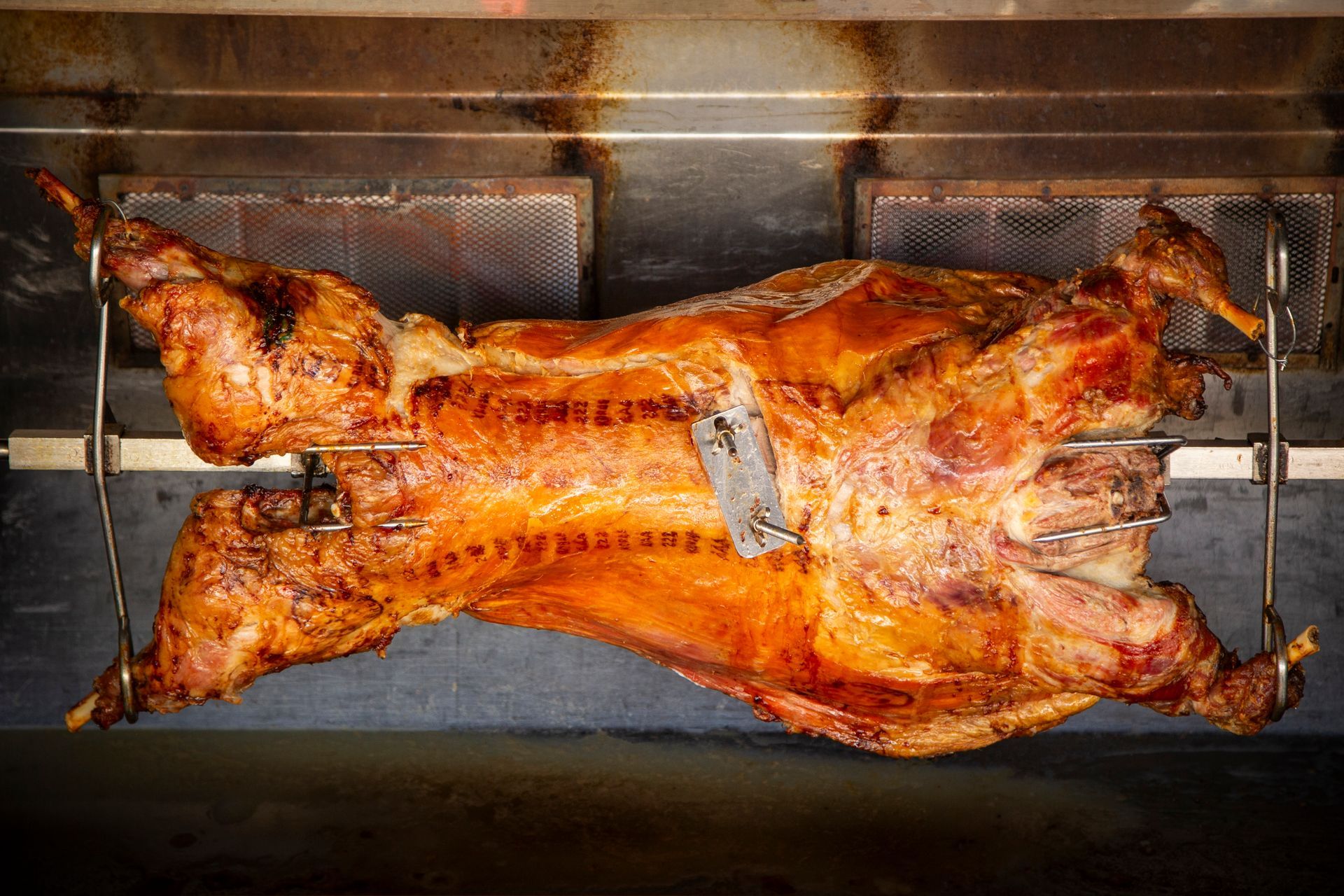 A whole roasted lamb turning on a rotisserie inside an oven.