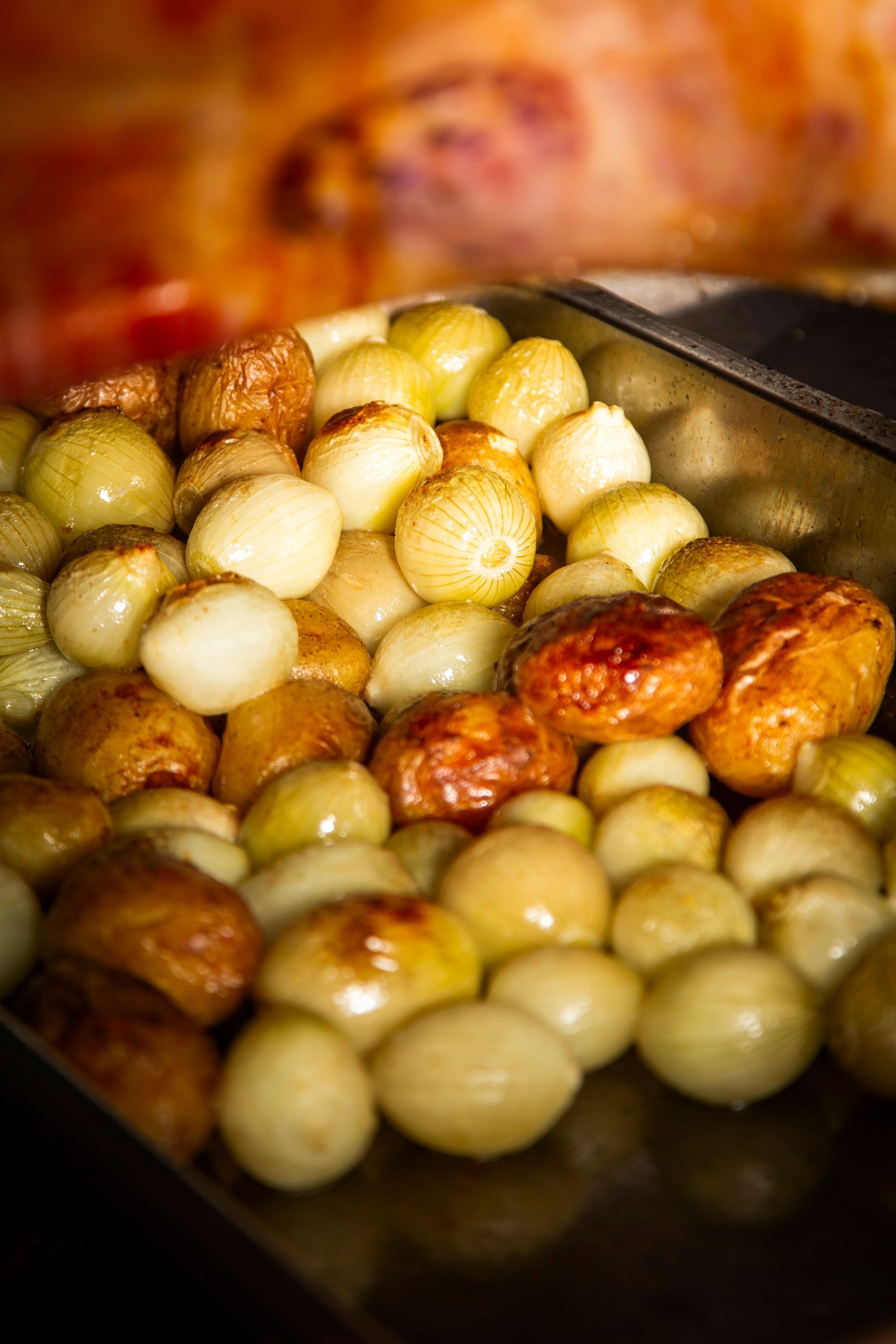 Roasted pearl onions in a metal tray, some browned, some pale, from a close-up perspective.
