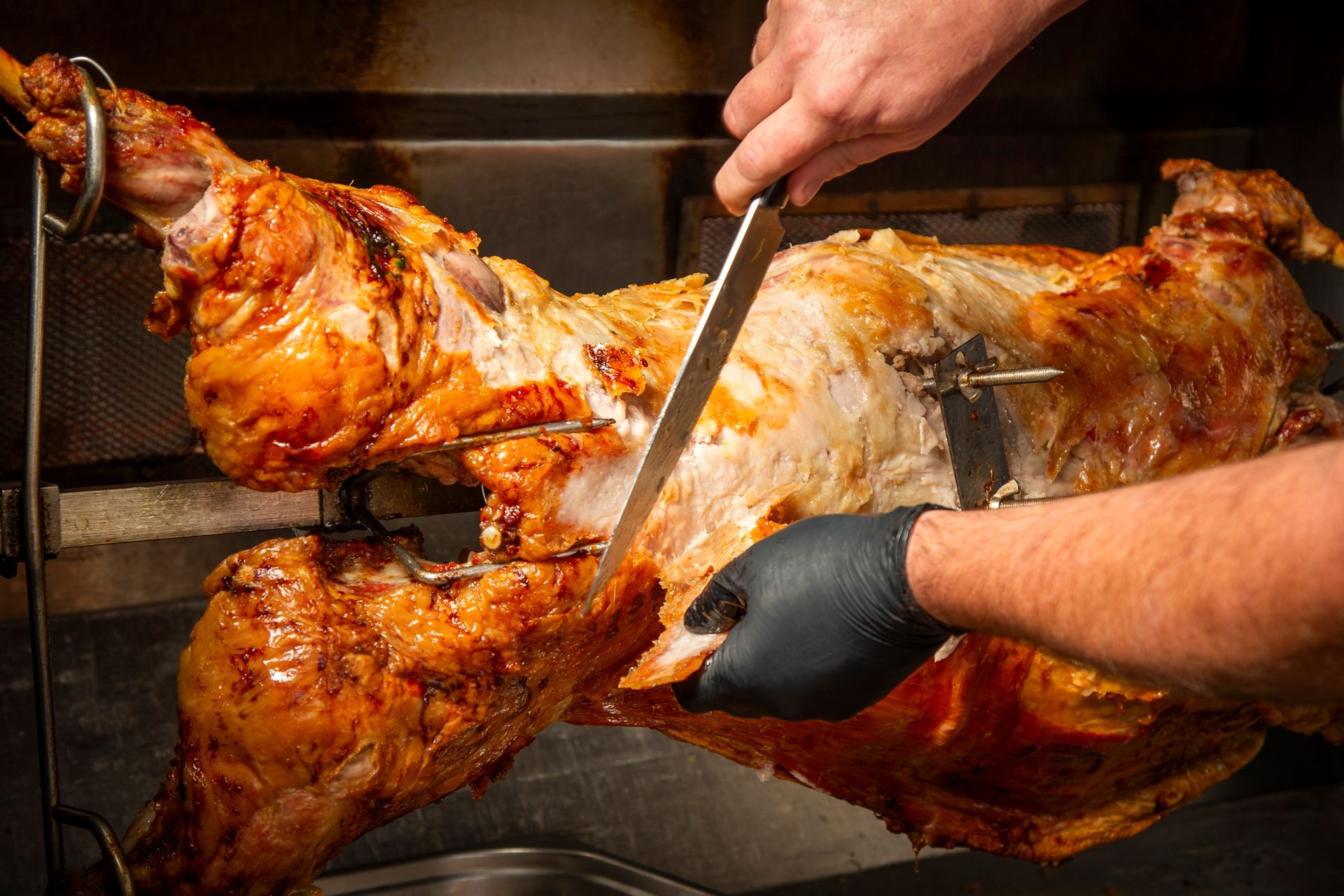 Roasted whole lamb being carved with a large knife, indoors.