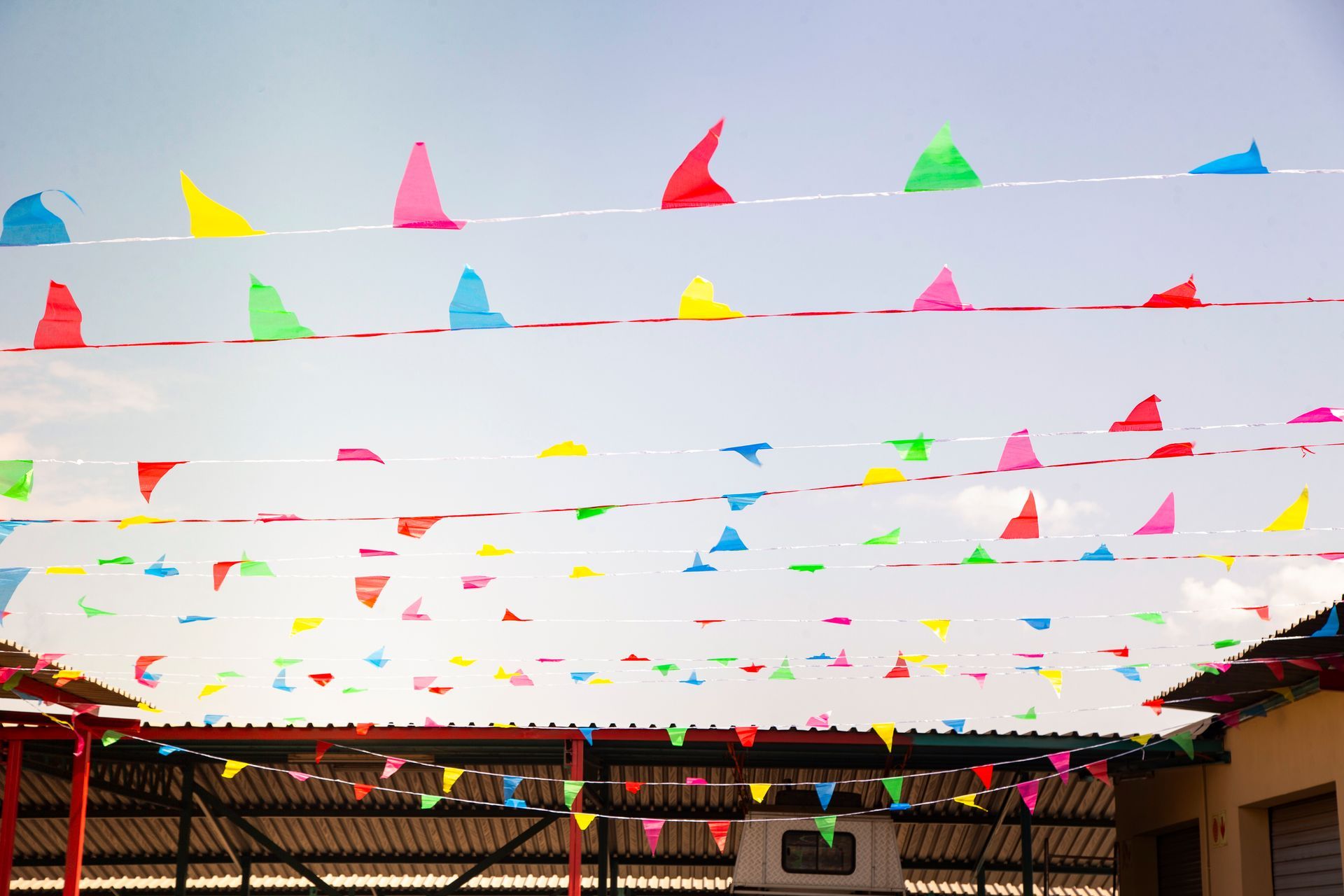 Colorful triangle flags strung across the sky, above a building with a metal roof.