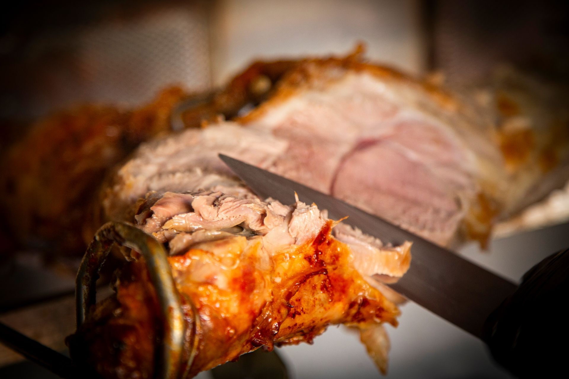 Roast pork being sliced with a knife; golden-brown skin, pink meat visible.