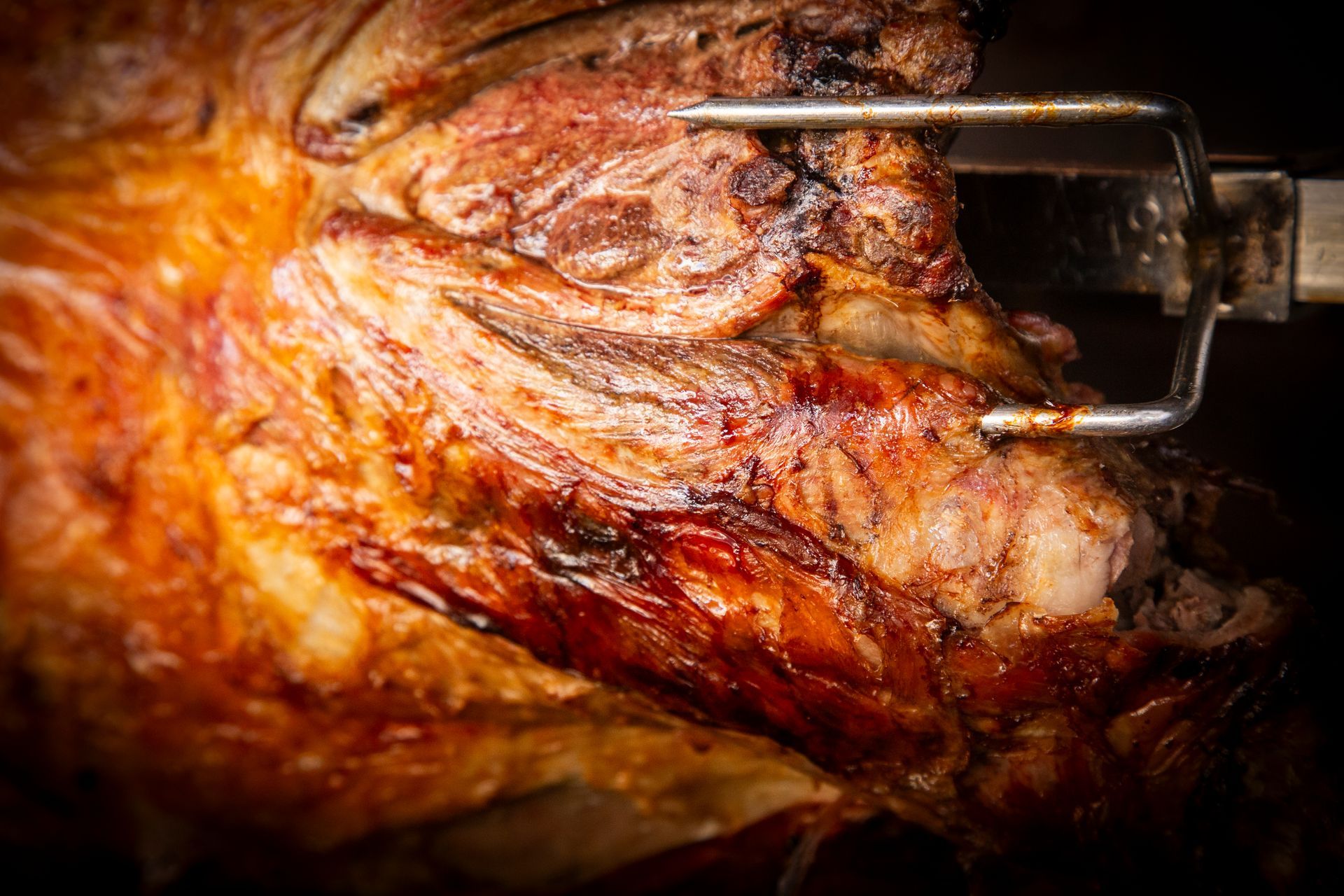 Roast lamb on a rotisserie, browned and juicy, held by metal prongs.
