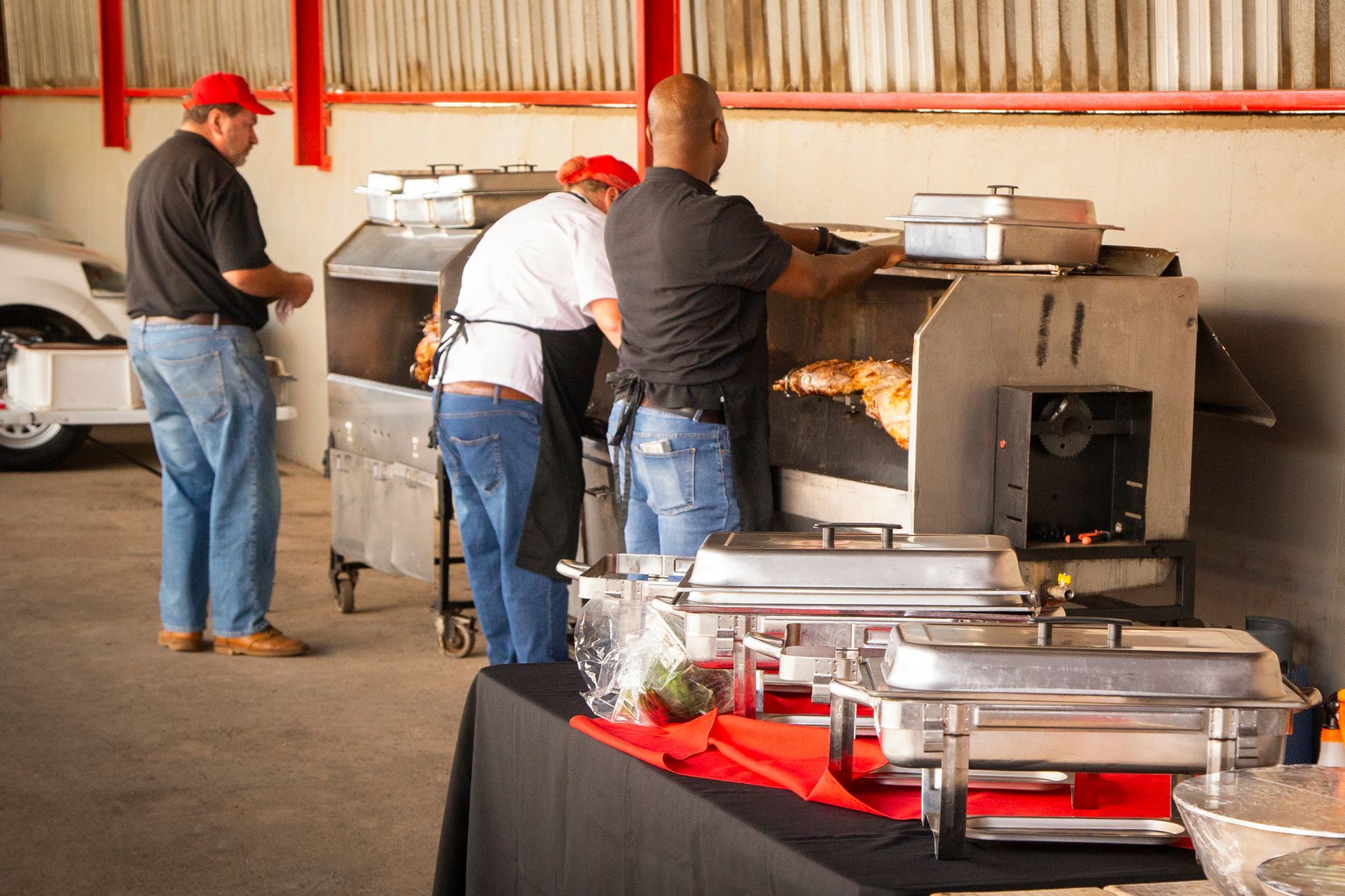 People cooking food outdoors with large metal smokers, food serving trays on a table.