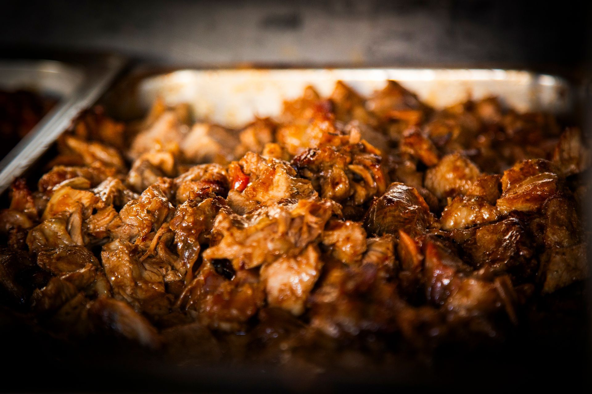 Cooked meat pieces in a metal tray, appearing brown with a glossy sheen.