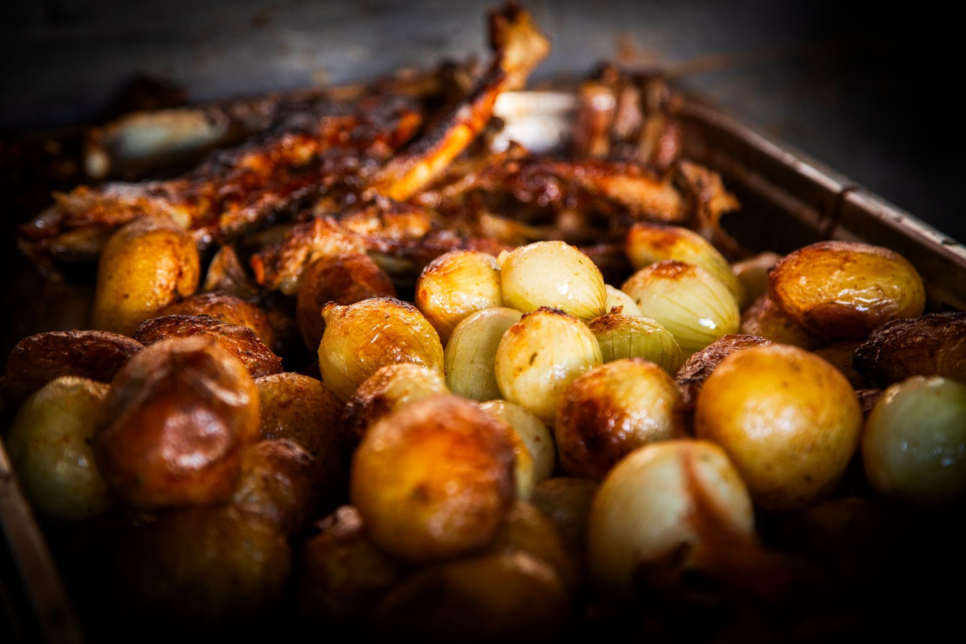 Roasted lamb ribs with potatoes and onions in a metal pan.