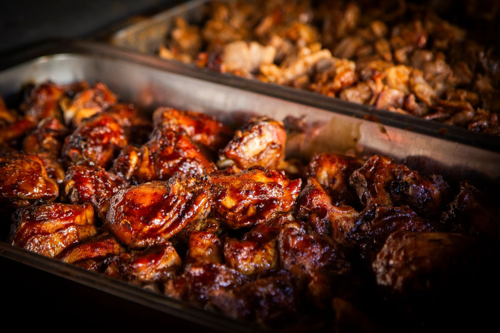 Chicken pieces coated in glossy red sauce in a tray, alongside a tray of darker meat.