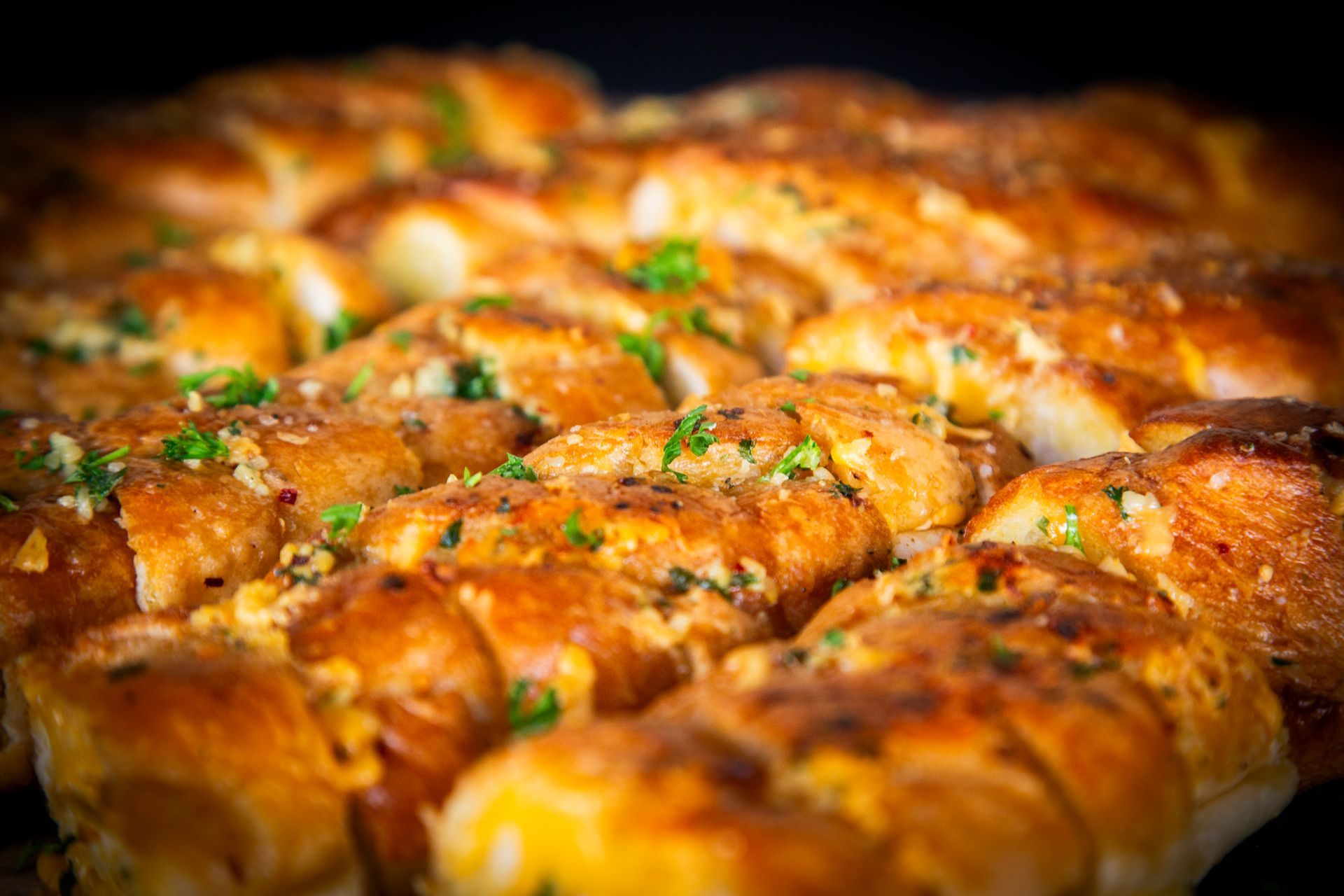 Golden-brown garlic bread rolls, close-up, with visible herbs and garlic topping.