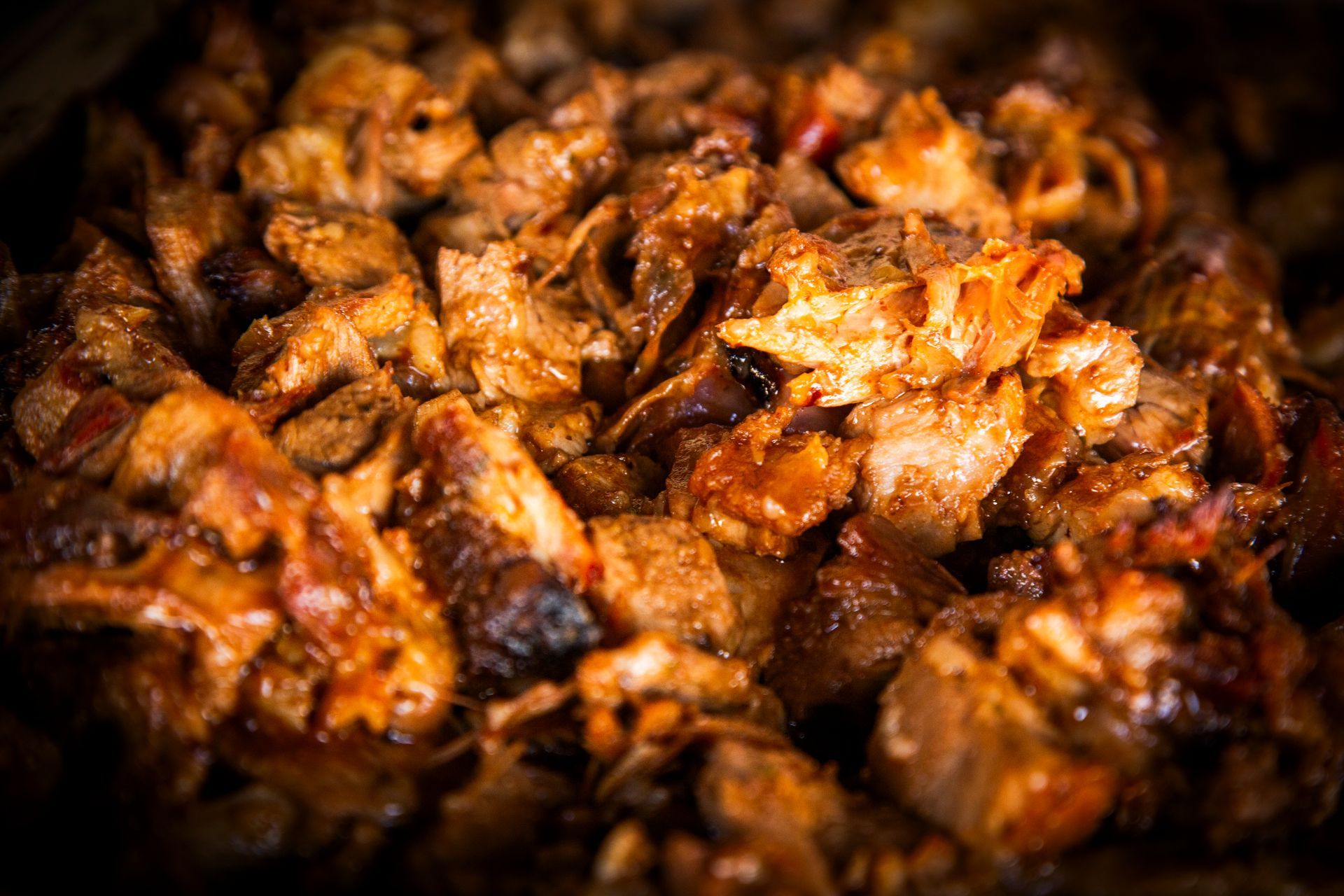 Close-up of cooked, seasoned meat, possibly pulled pork, with rich brown and reddish hues.