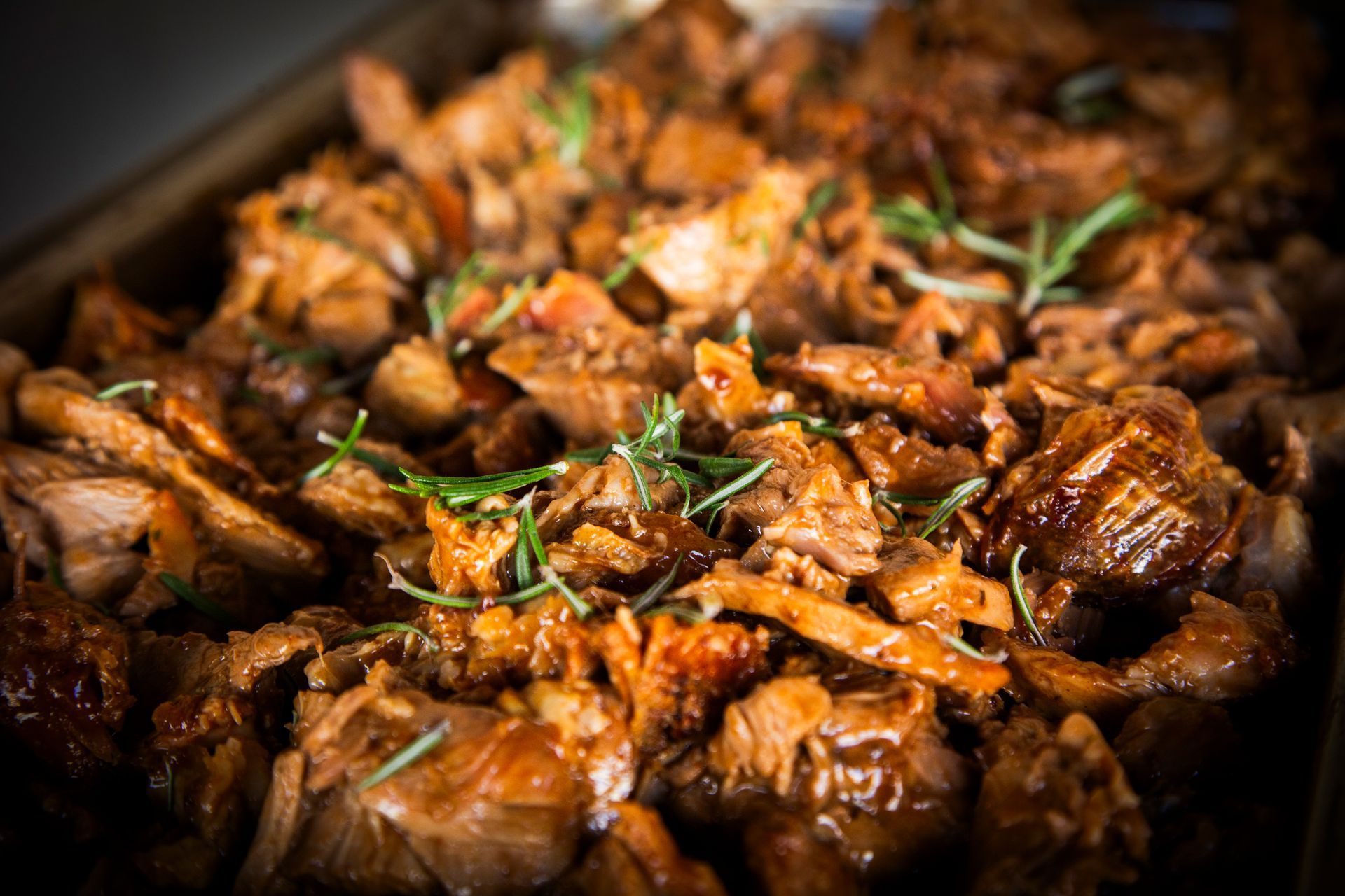 Close-up of cooked pulled pork with rosemary garnish in a baking dish.
