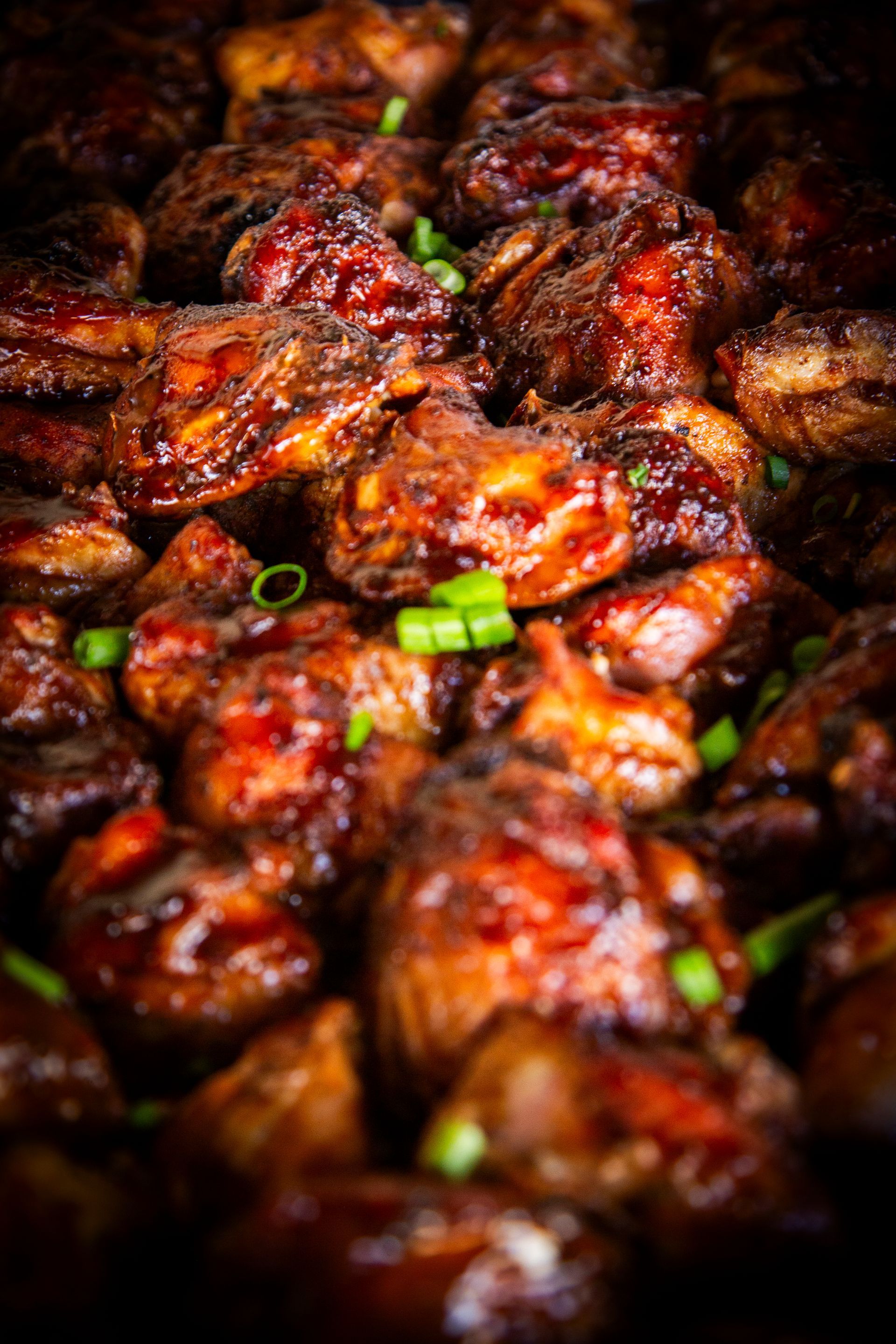 Close-up of glistening, glazed chicken pieces sprinkled with green onions.