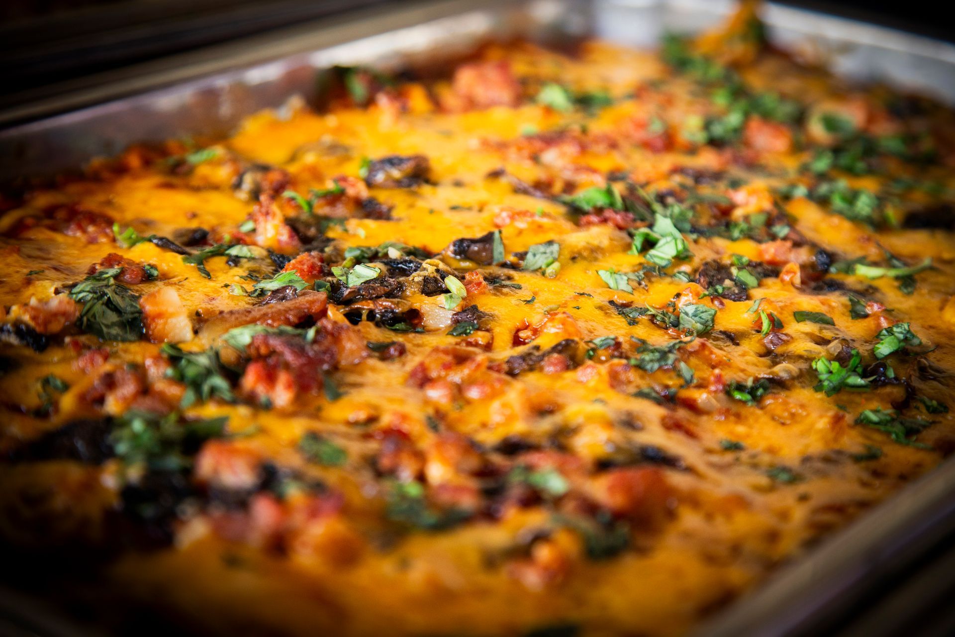 Casserole with melted orange cheese, red chunks, and green herbs in a metal pan.
