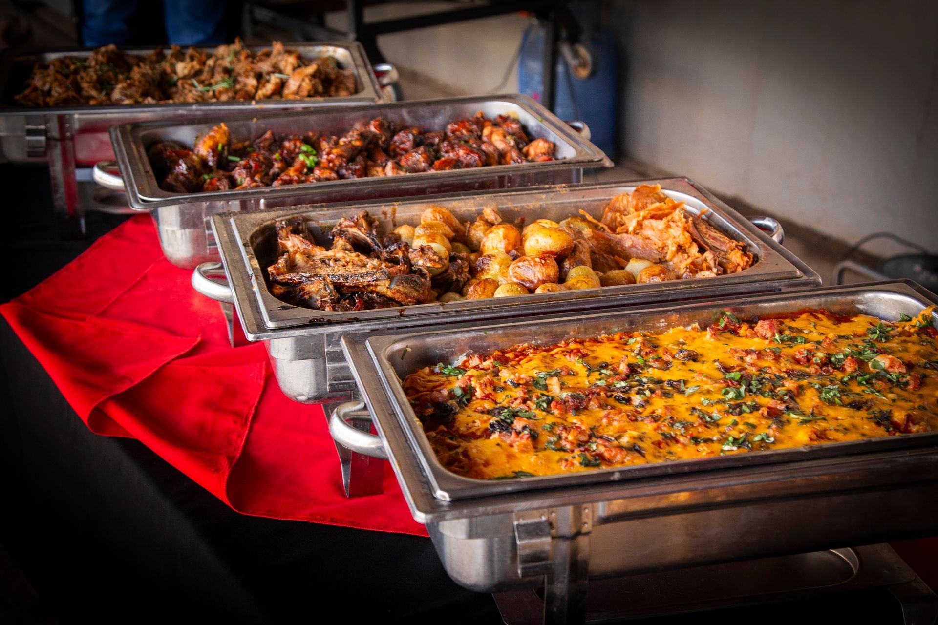 Buffet with various dishes in chafing dishes on a red tablecloth, ready to serve.