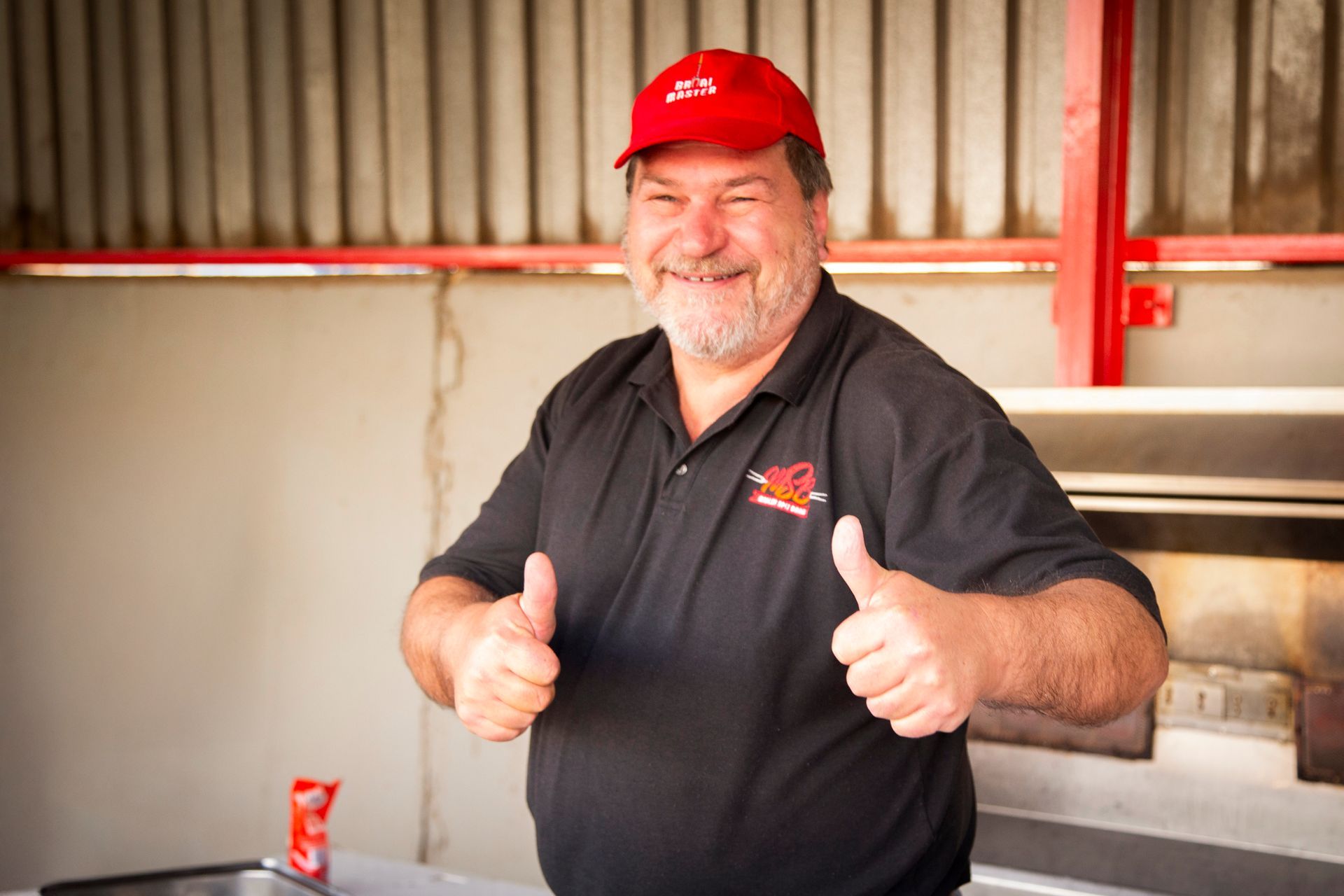 Man in red cap and black shirt gives thumbs up; outdoor setting.