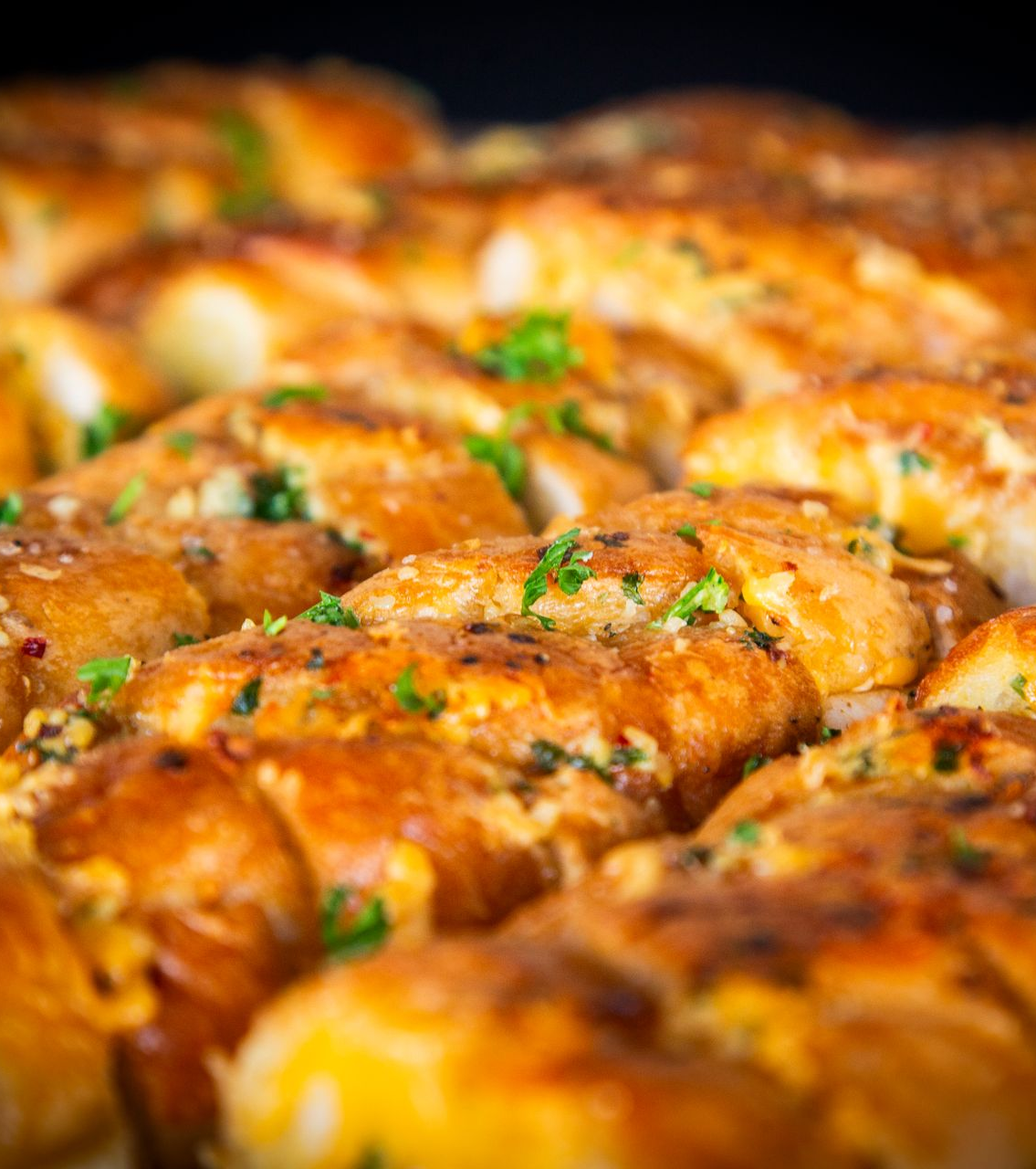 Close-up of golden-brown, baked garlic knots topped with parsley, ready to eat.