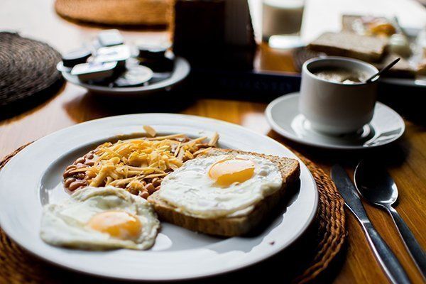 Breakfast plate with fried eggs, beans, cheese, toast, coffee, and utensils on a table.