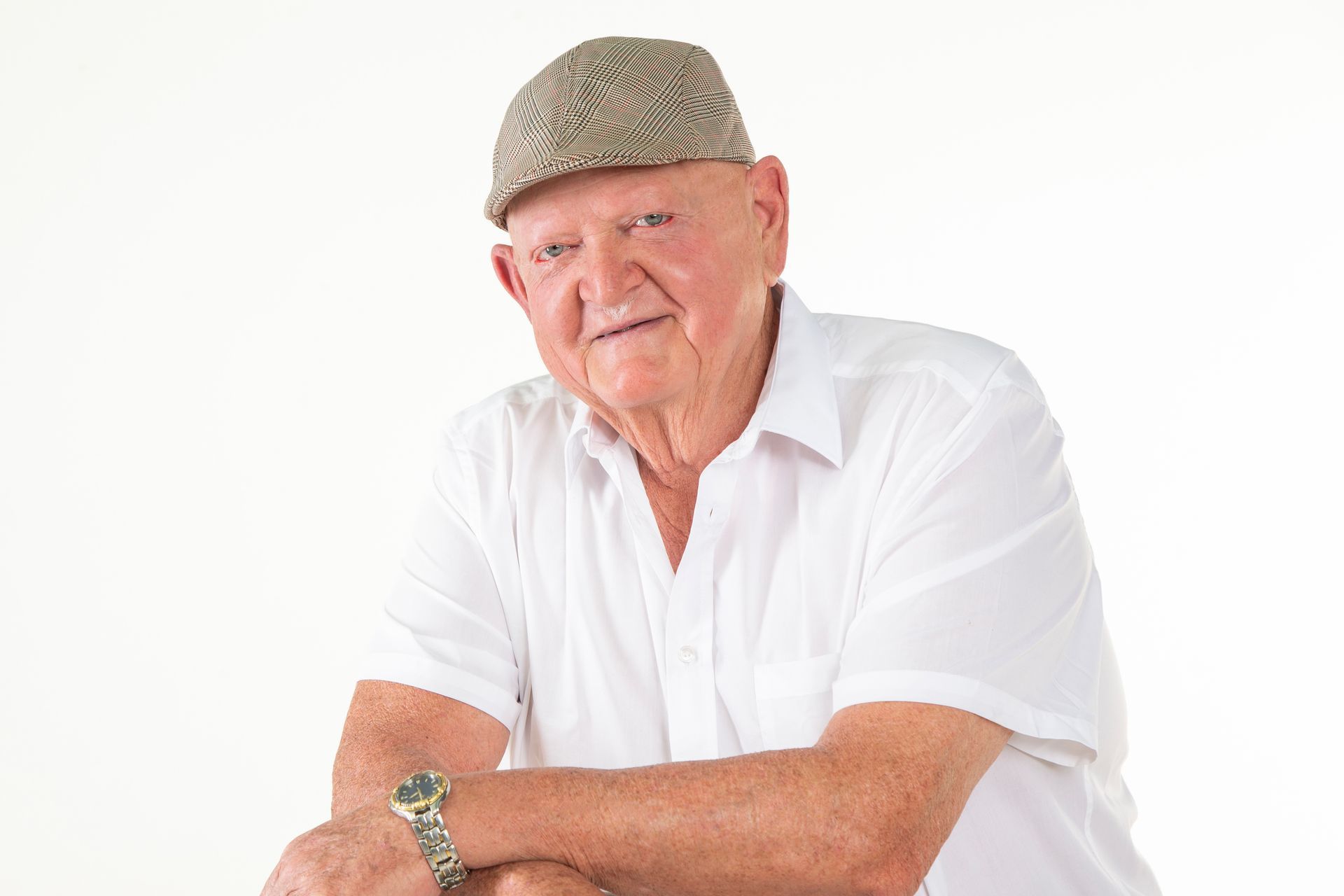 Elderly man wearing a cap, white shirt, and watch, smiling. White background.