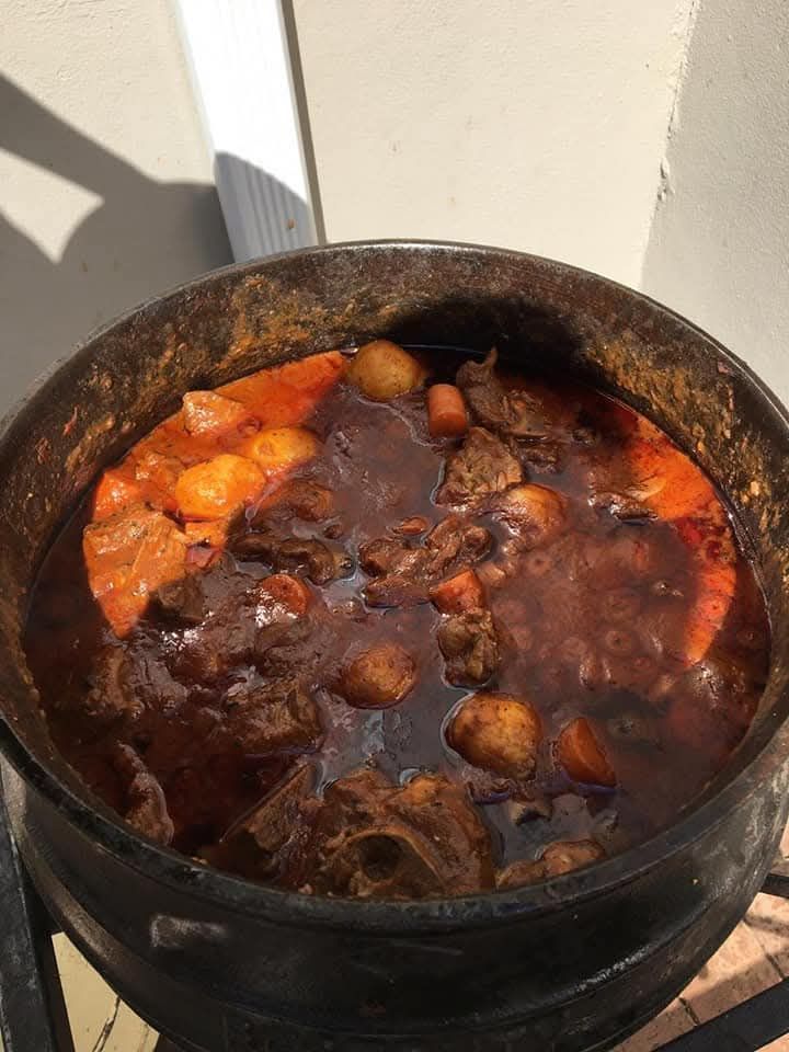 Potjie stew in a large black pot, with potatoes, carrots, and meat.
