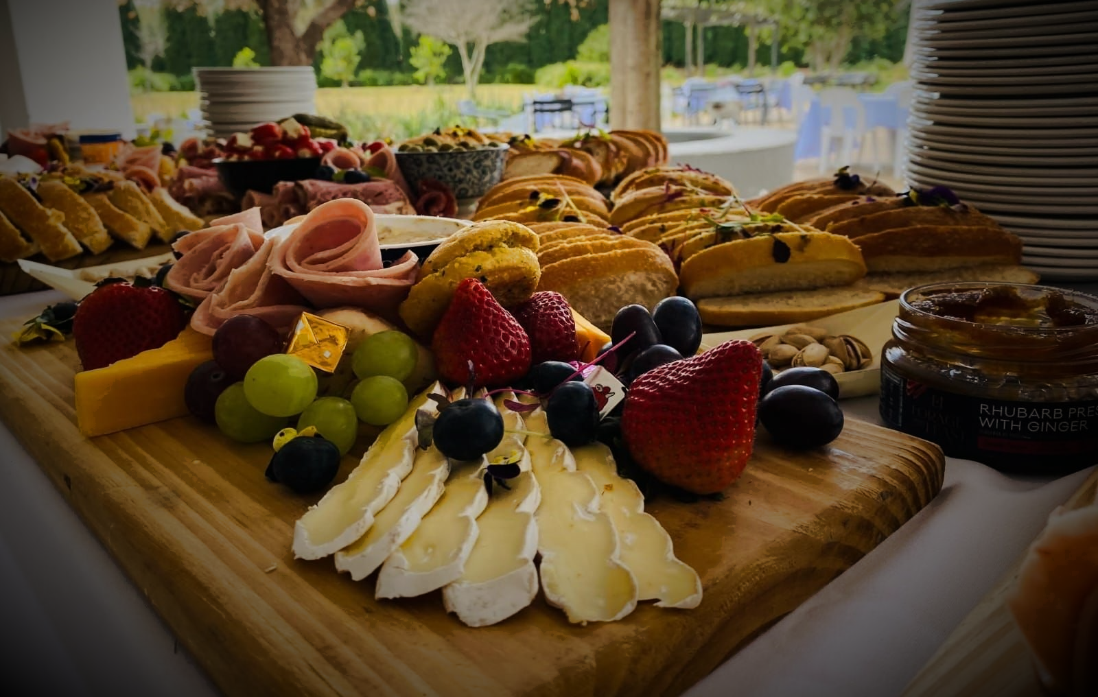 Charcuterie board with cheese, fruit, meats, bread, and toppings, outdoors.