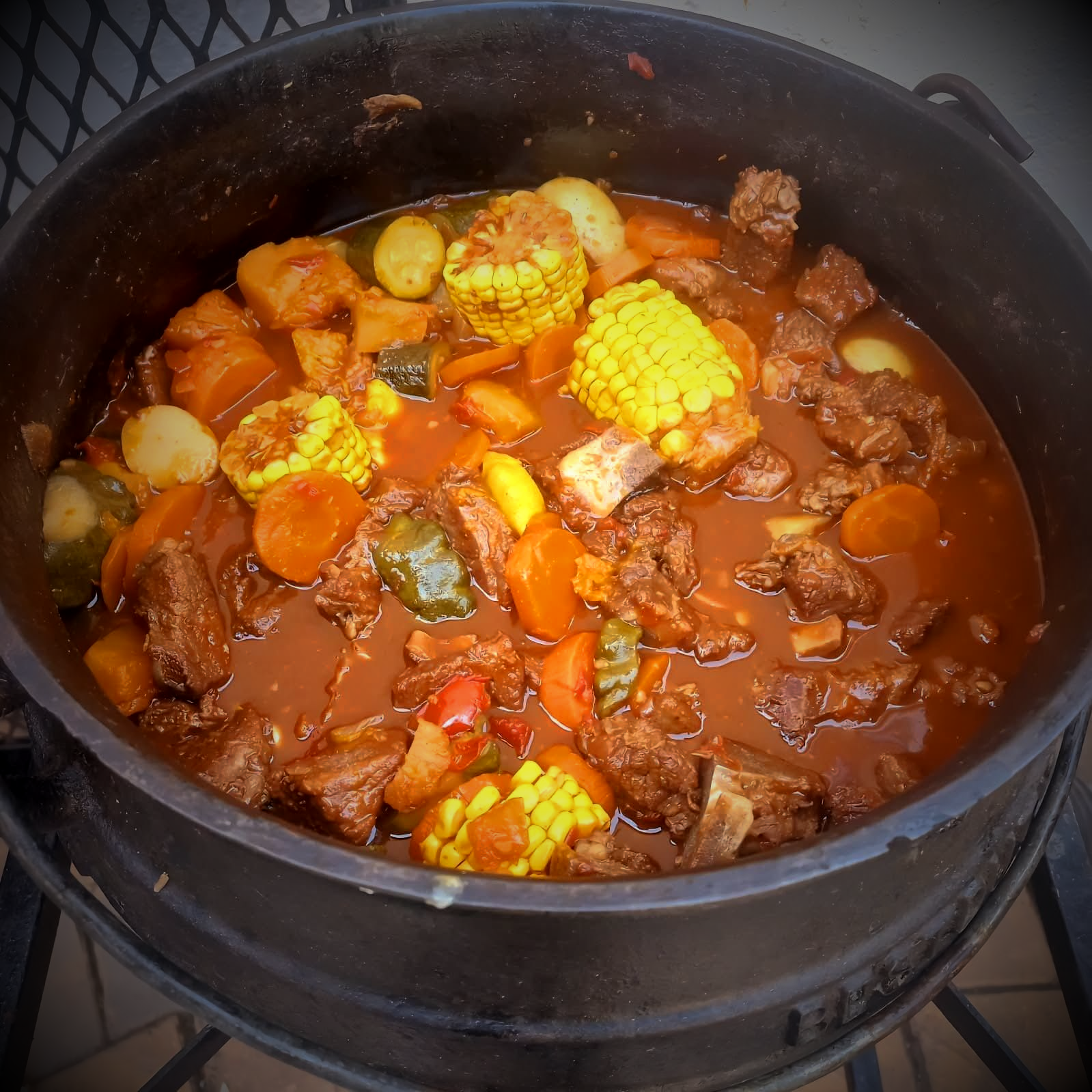 Beef stew with vegetables, including corn, in a large black pot.