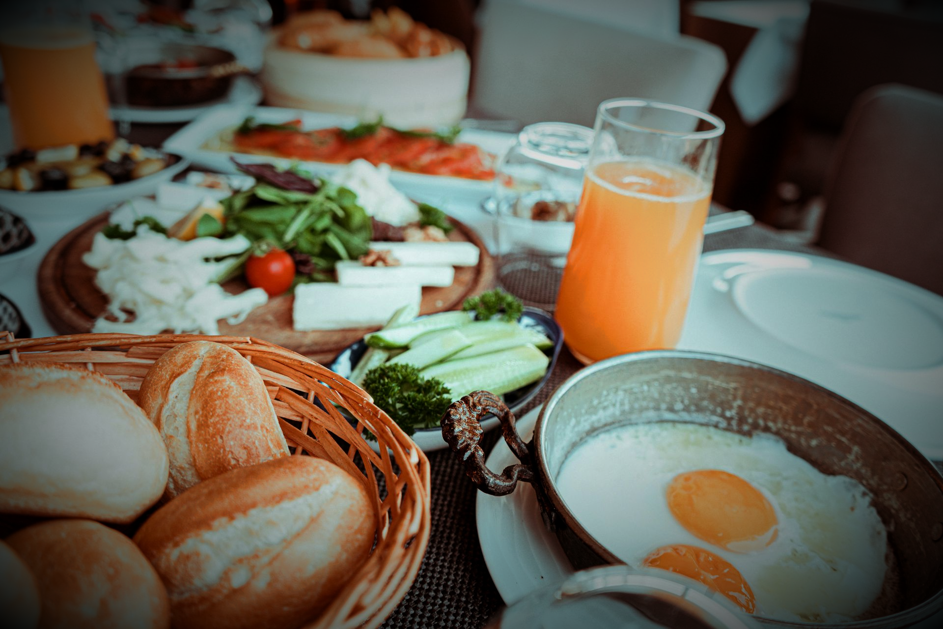 Breakfast spread: bread basket, eggs, cheeses, vegetables, and orange juice on a table.