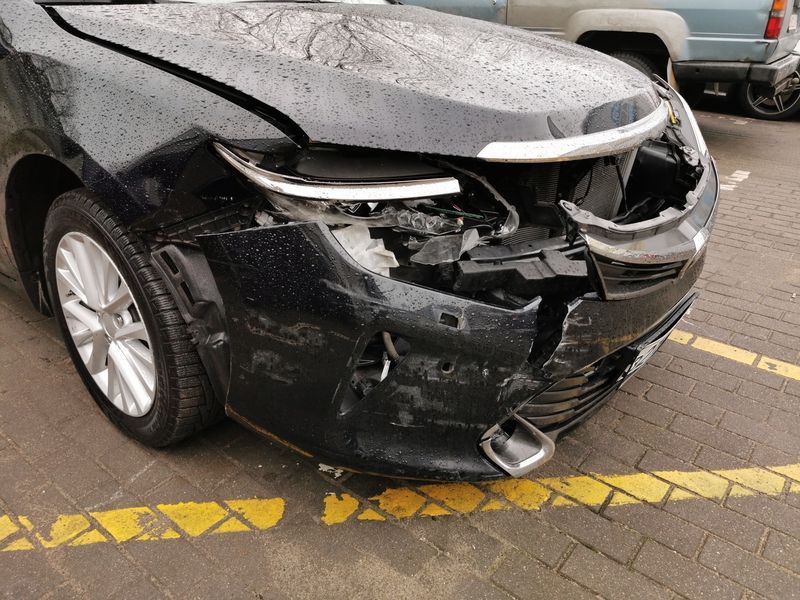 A black car with a damaged front end is parked in a parking lot.