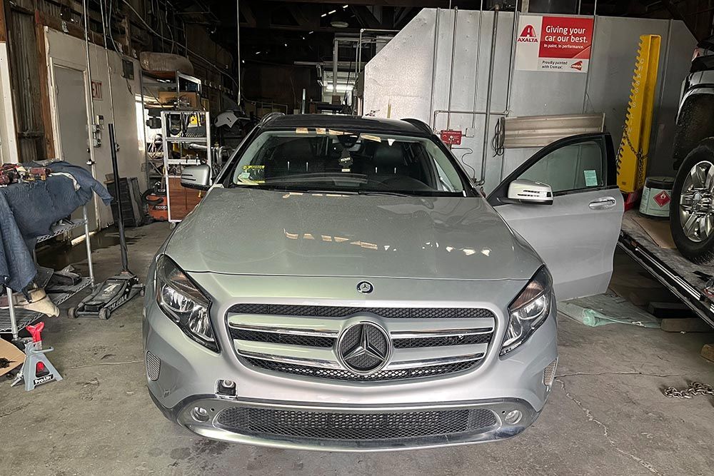 A silver mercedes benz is sitting on a tow truck in a garage.
