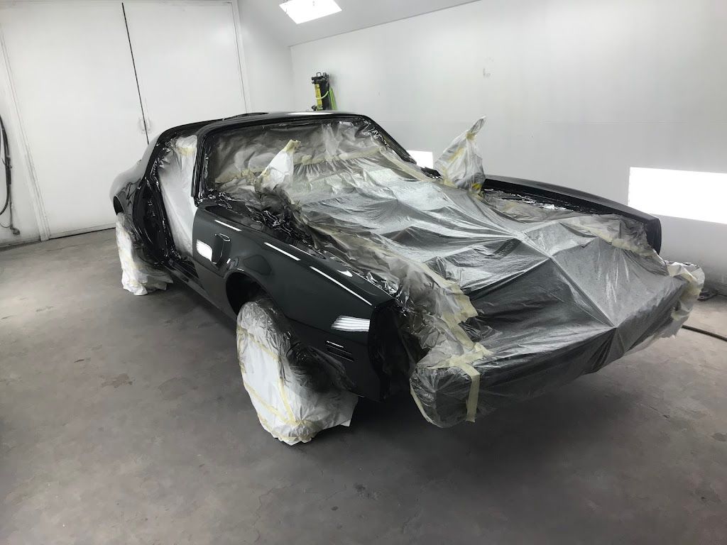 A black car is sitting in a paint booth covered in plastic.