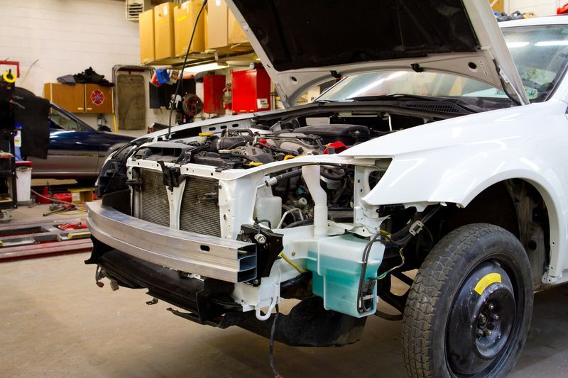 A white car with the hood open is being worked on in a garage.