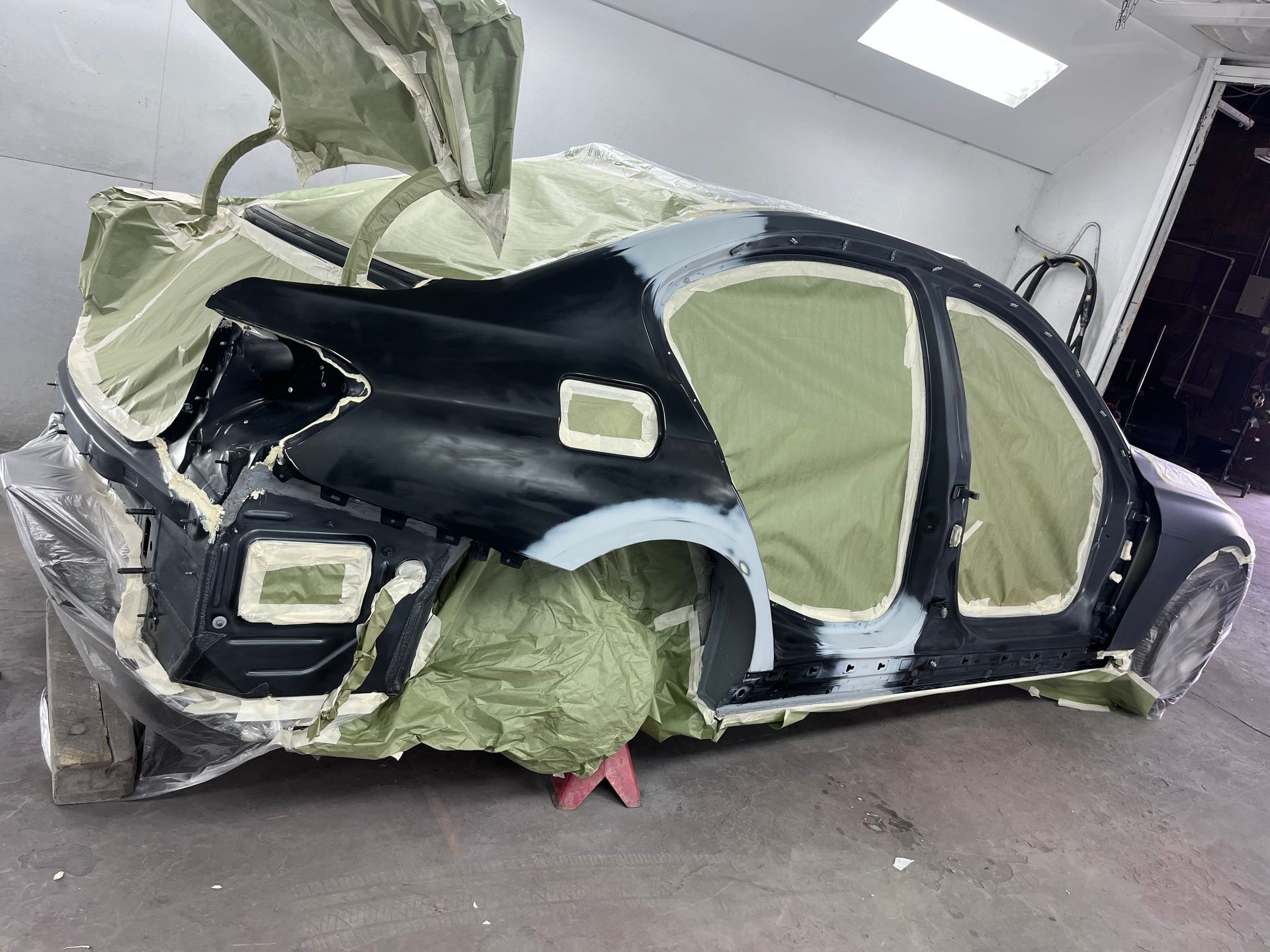 Car partially covered in protective material, undergoing bodywork and painting in a workshop.