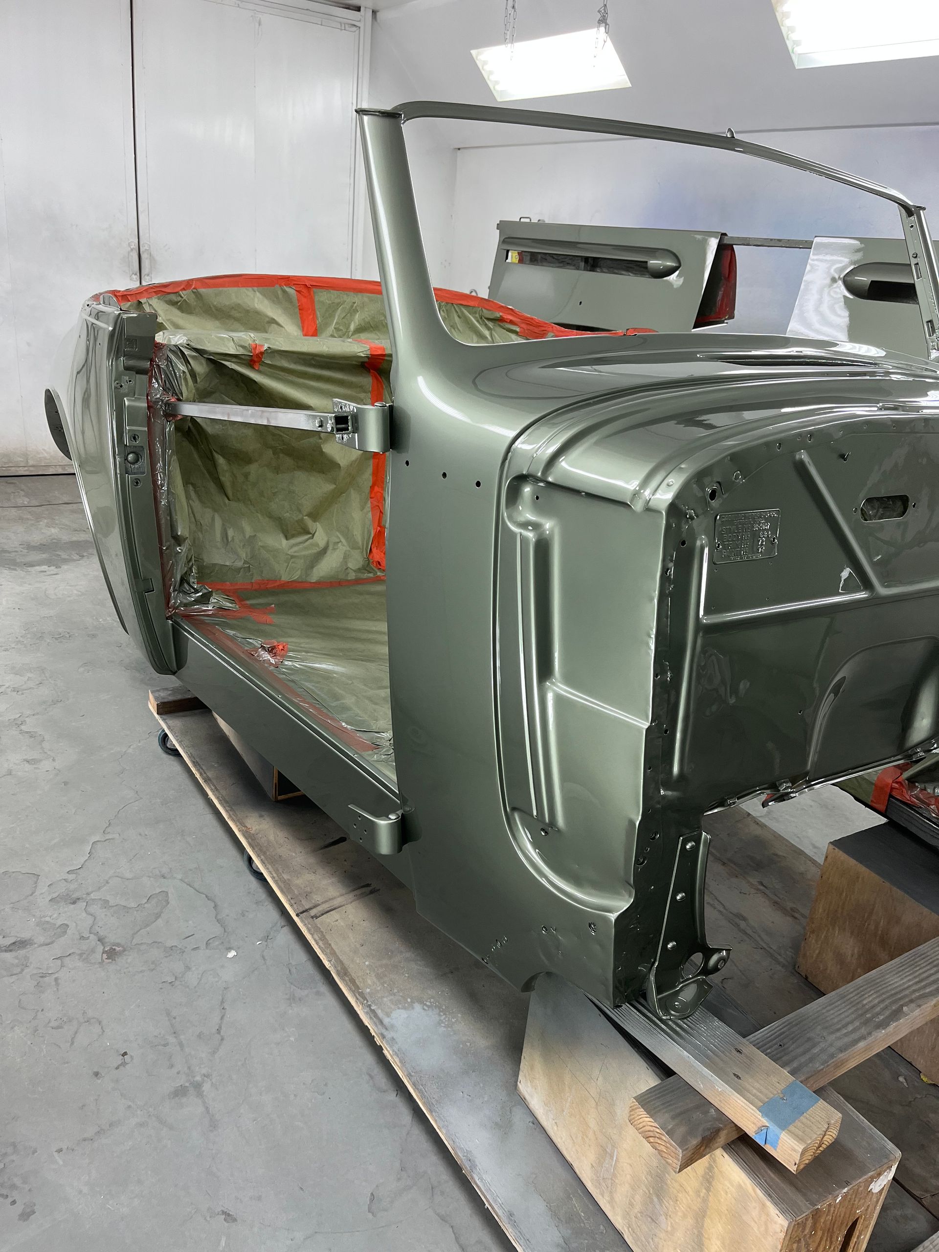 Green car body in a workshop, doors open, covered in orange tape.