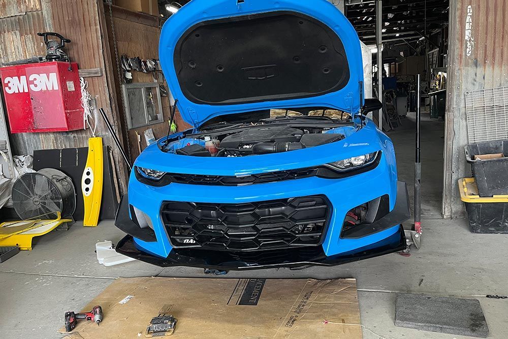 A blue car with the hood open is sitting in a garage.