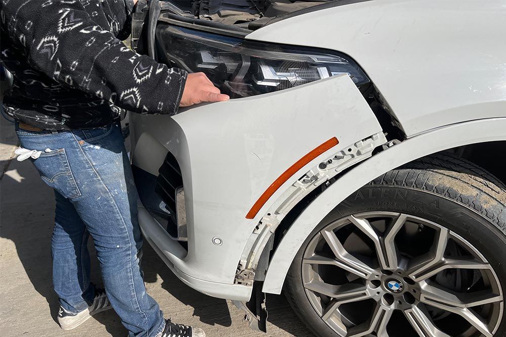 A man is looking under the hood of a white car.