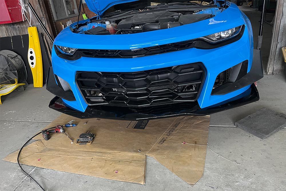 A blue car is sitting on a piece of cardboard in a garage.
