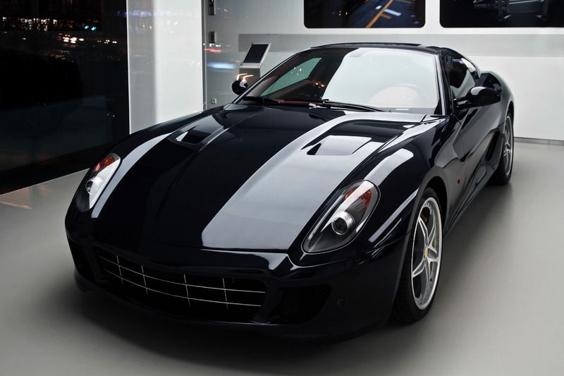 Black Ferrari sports car in a showroom, glossy finish, gray interior and floor.