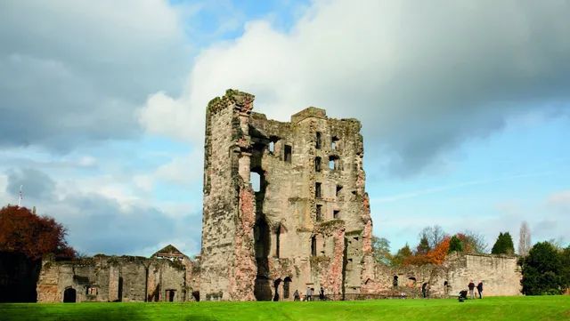 The ruins of a castle are in the middle of a grassy field.