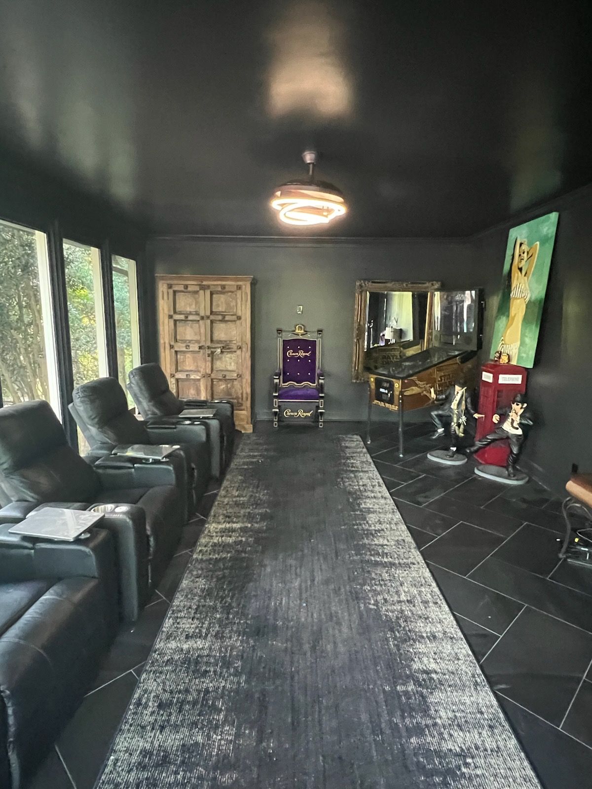 Modern black lounge with leather seating, central rug, mirror, and a purple chair at the far end.