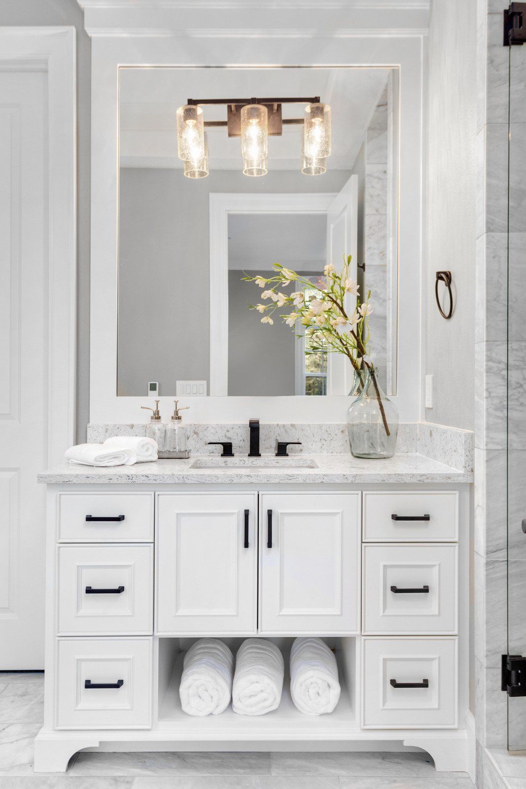 A bathroom with white cabinets , a sink , a mirror and towels.