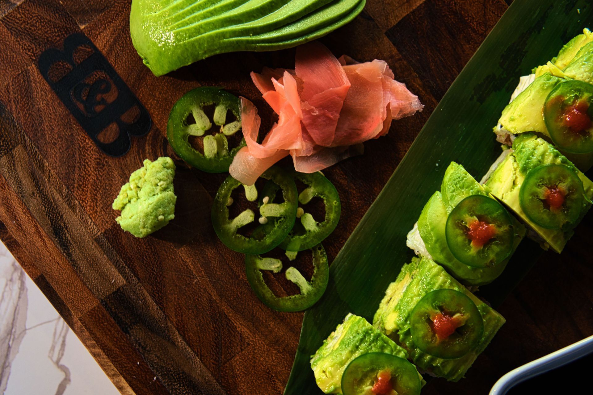 A wooden cutting board topped with avocado , jalapenos , and ginger.