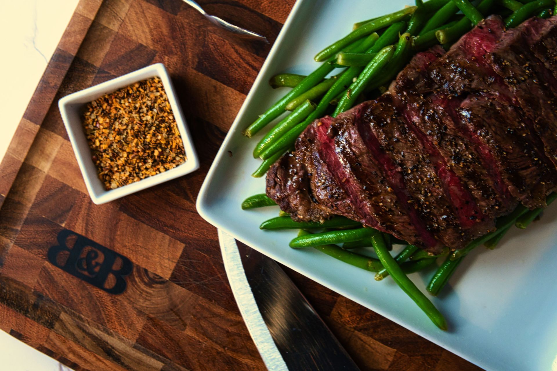 A steak and green beans on a white plate on a wooden cutting board