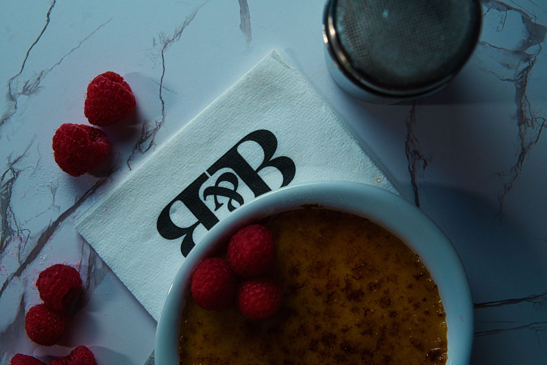 A bowl of food with raspberries and a napkin with the letter b on it.