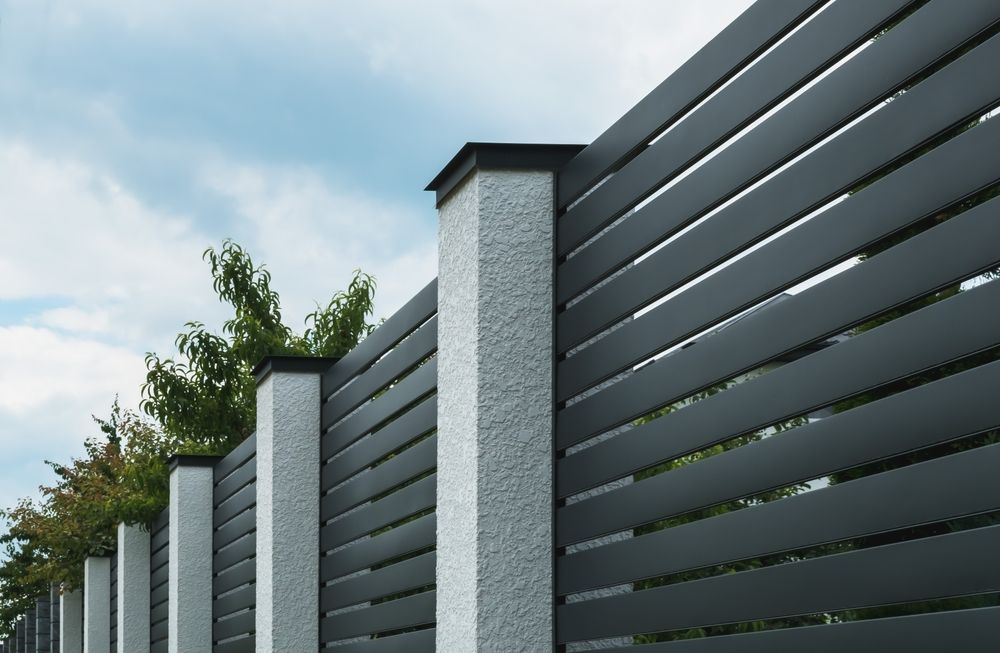 Gray horizontal slat fence with stucco posts capped in black against a cloudy sky.