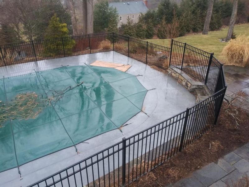 An aluminum fence surrounds a swimming pool with a green cover on it.