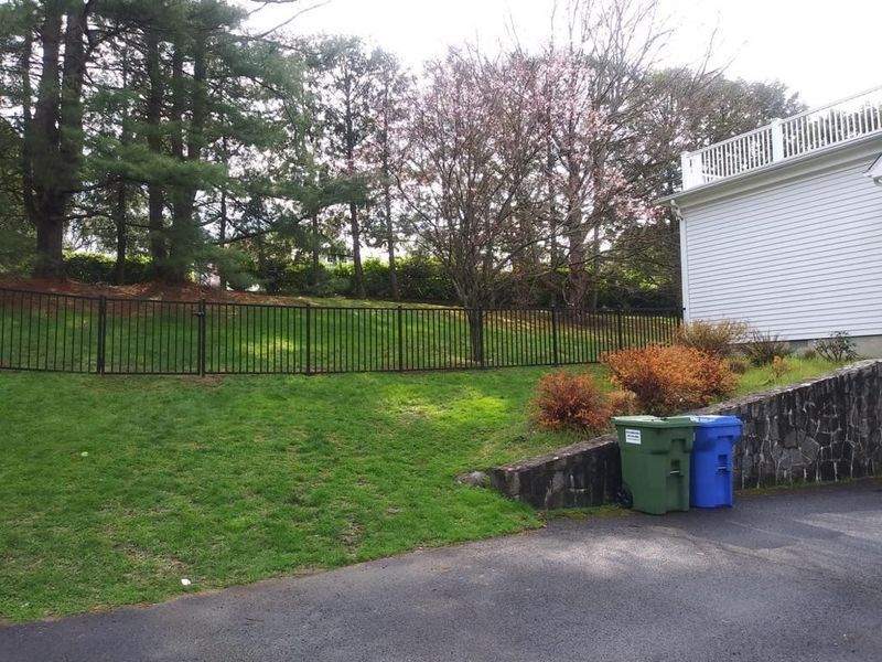 A white house with a fence and trash cans in front of it
