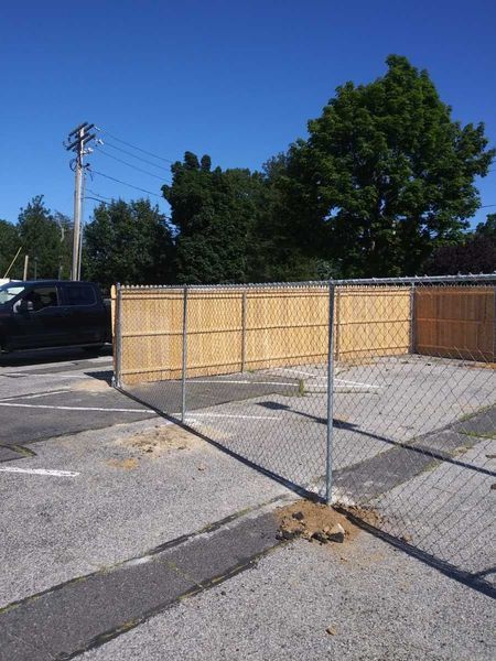 A chain link fence with a wooden fence in the background
