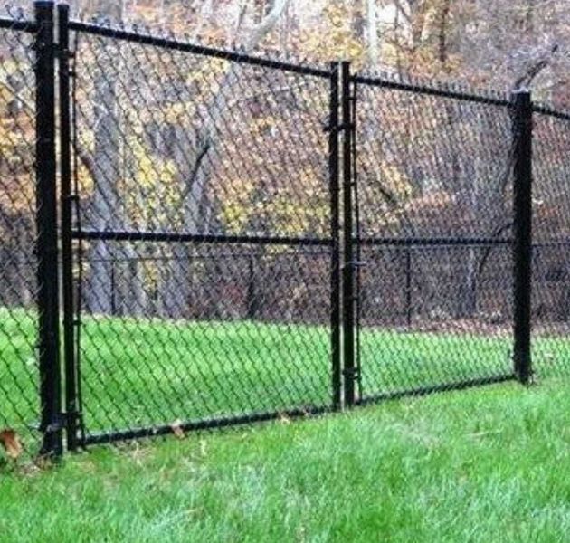 A chain link fence with a gate is in the middle of a lush green field.