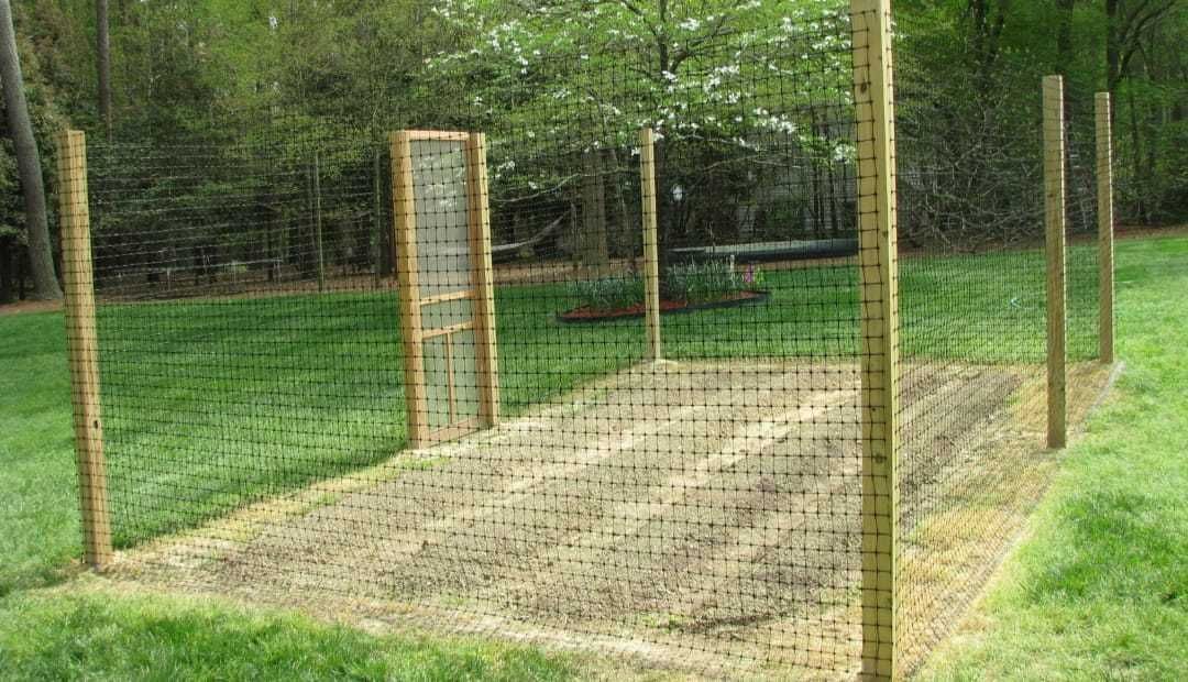 A garden with a fence around it and a picnic table in the background.